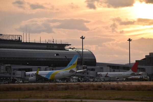 夕方の空を背景に空港の建物と飛行機が逆光で写る写真